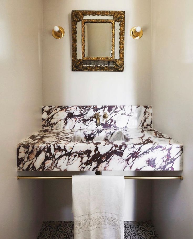 a bathroom with marble counter top and gold mirror on the wall above it, along with black and white tile flooring