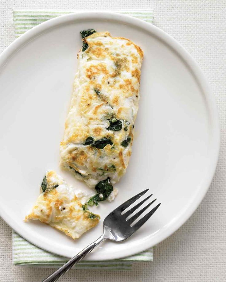 an omelet with spinach and cheese on a plate next to a fork