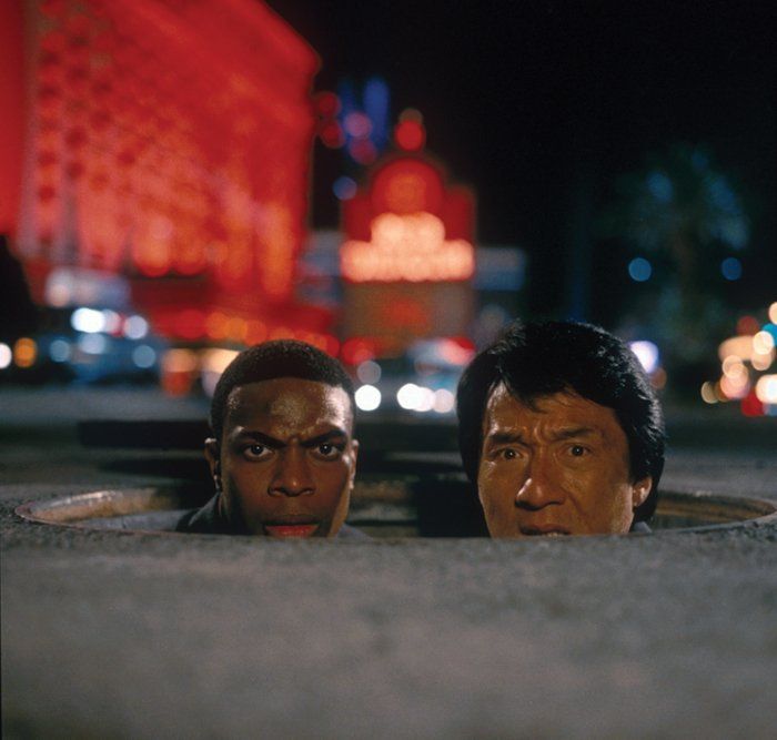 two men laying on the ground in front of a city street at night with neon lights behind them