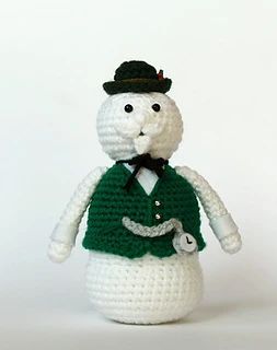 a crocheted snowman is wearing a green vest and black hat with a pipe