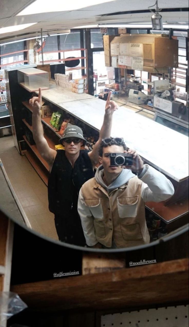 two men standing in front of a food counter taking a selfie with their cell phone