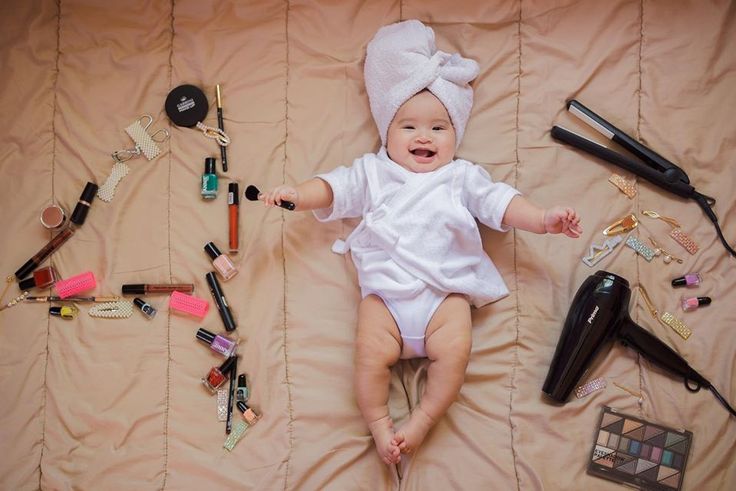 a baby laying on top of a bed with lots of makeup and hair accessories around it