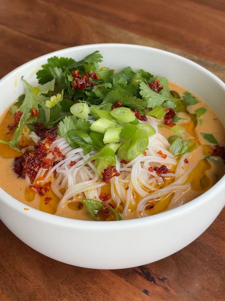 a white bowl filled with soup and veggies on top of a wooden table