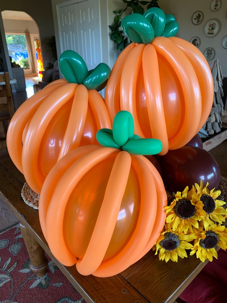 three pumpkin balloons sitting on top of a table next to sunflowers and vases