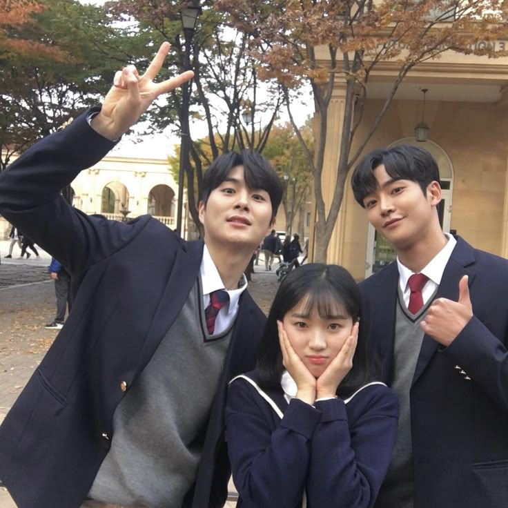 three young people posing for the camera in front of a building with two fingers up