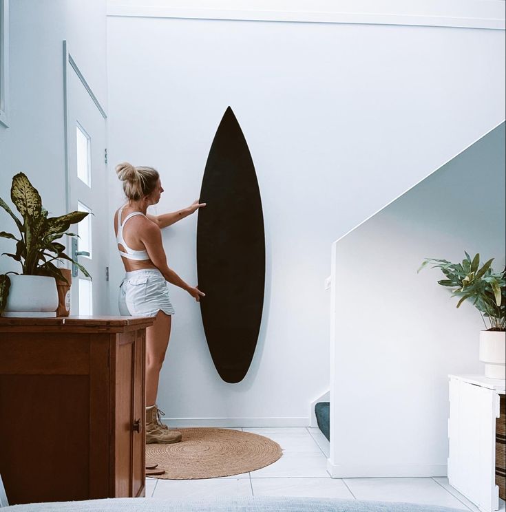 a woman standing next to a black surfboard on a wall in a living room