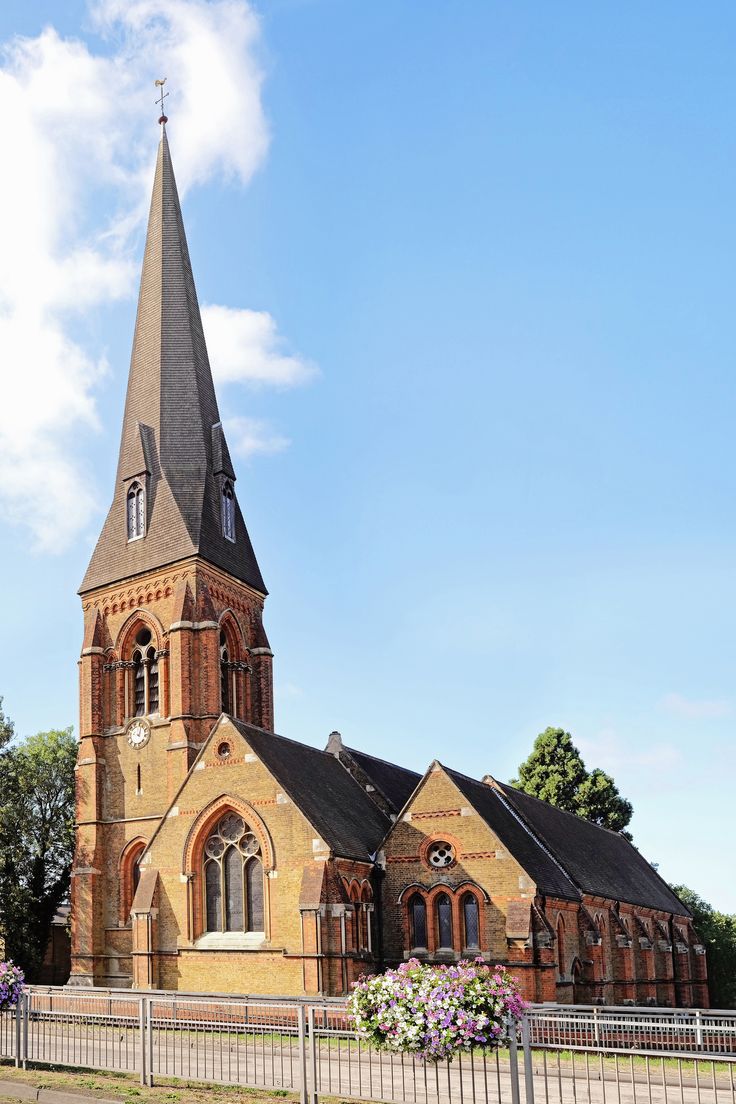 an old brick church with a steeple on the top and flowers in the foreground