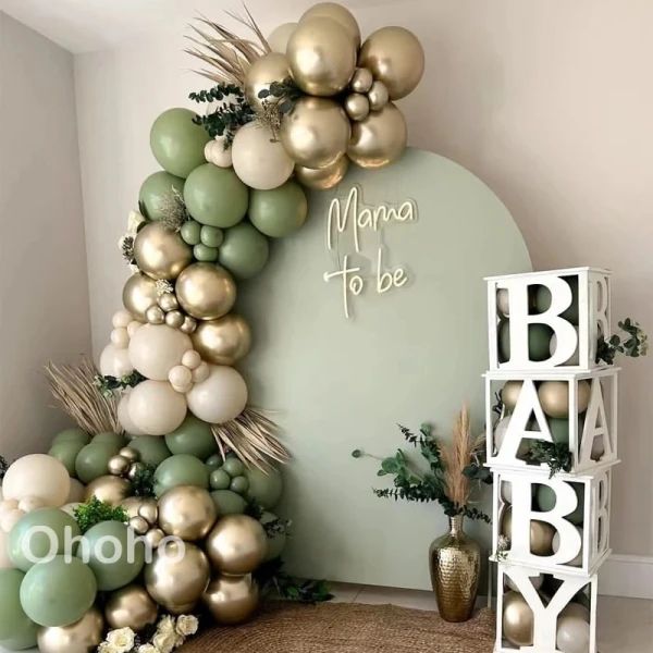 a baby shower is decorated with gold and green balloons, greenery, and white letters