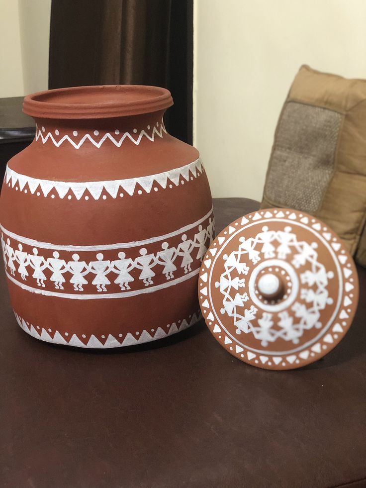 a brown and white vase sitting on top of a table next to a small plate