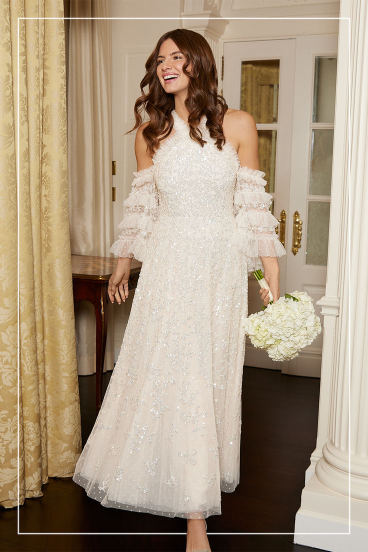 a woman in a white dress holding a bouquet and smiling at the camera while standing next to a doorway