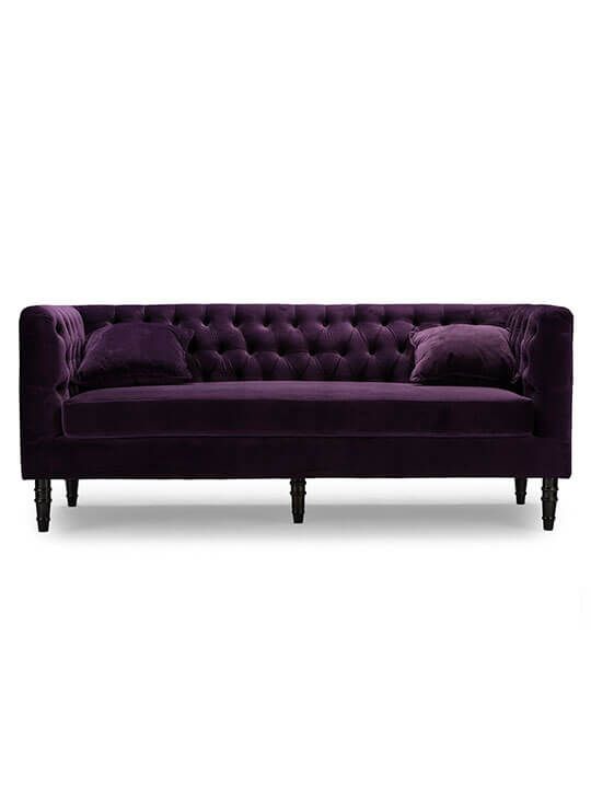 a purple velvet couch with two pillows on it's back and one arm extended