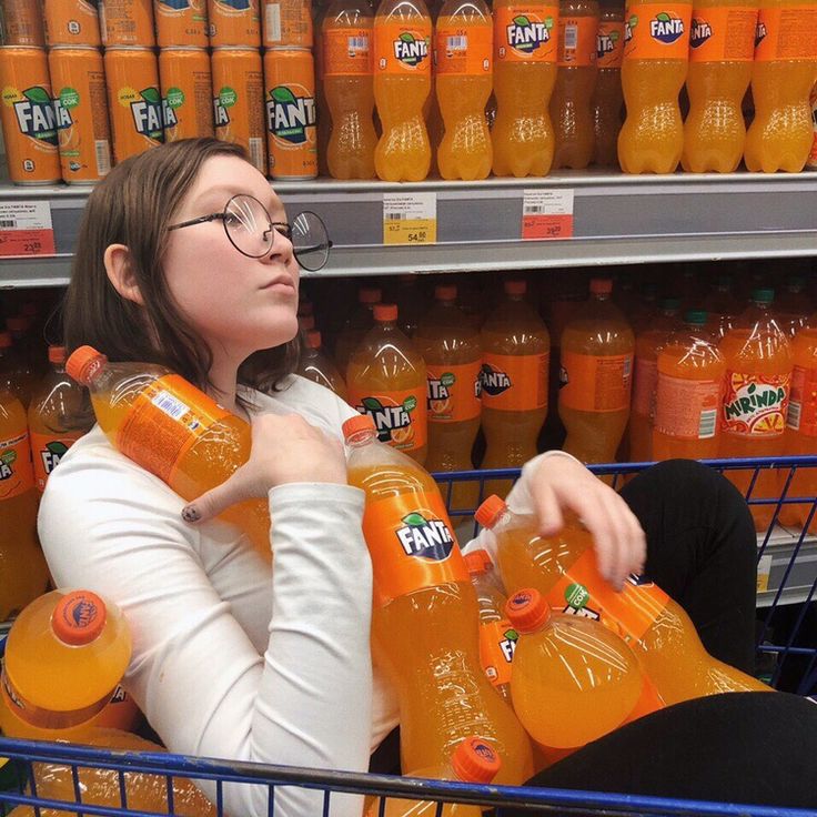 a woman sitting in a shopping cart with orange juice bottles on the shelf behind her