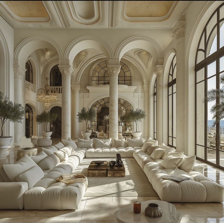 a large living room filled with lots of white furniture and tall arched windows on the wall