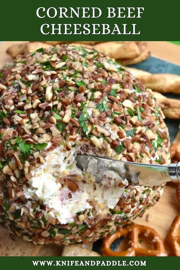 a close up of a cheese ball on a cutting board with pretzels in the background