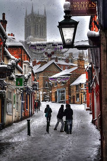 two people walking down a snowy street in front of a building