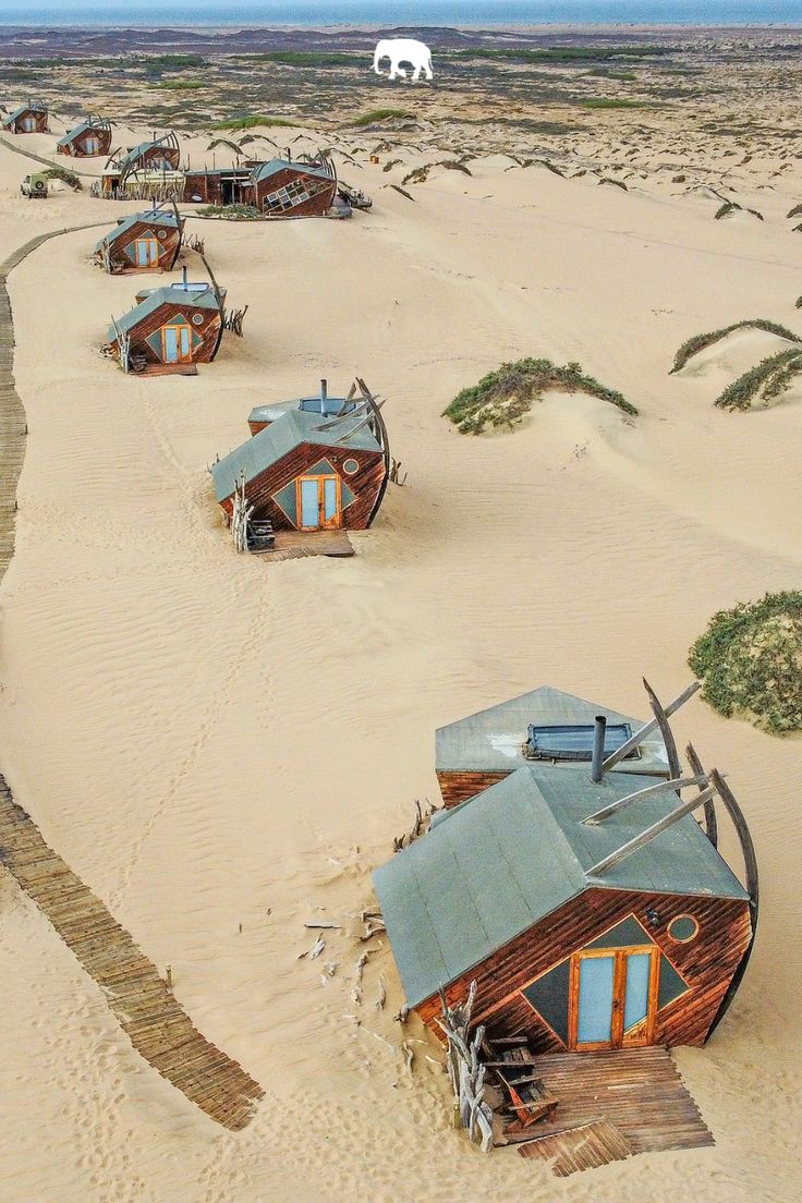 an aerial view of several small wooden houses in the sand with elephants walking around them