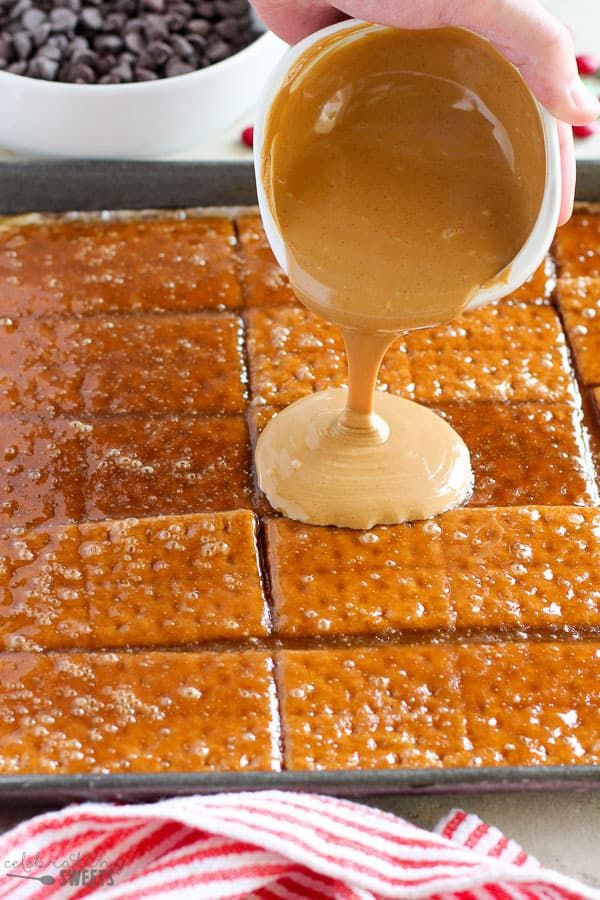 someone pouring caramel sauce on top of crackers in a baking pan with chocolate chips