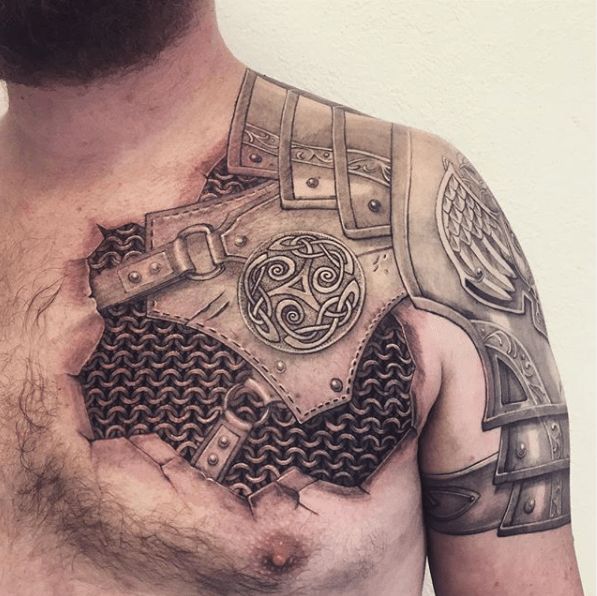 a man with tattoos on his chest and chest is holding a piece of metal in the shape of a shield