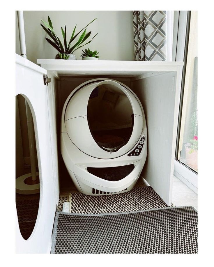 a white dog house with a cat in it's kennel and plants on the window sill