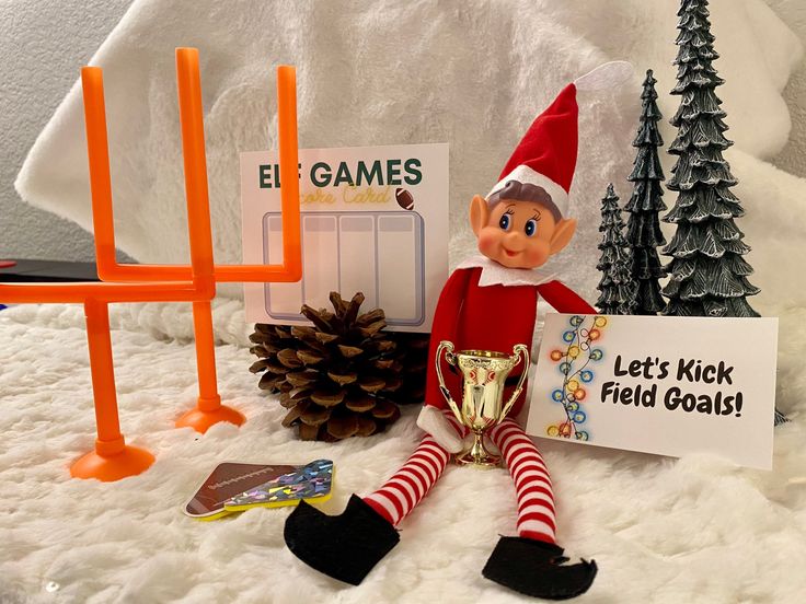 an elf is holding a trophy next to a sign and some pine cones on the snow