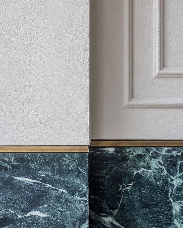 the corner of a room with marble and gold trimmings on the wall, next to a white door