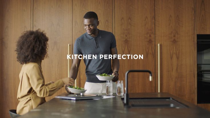 a man and woman standing in front of a kitchen counter with a bowl of food