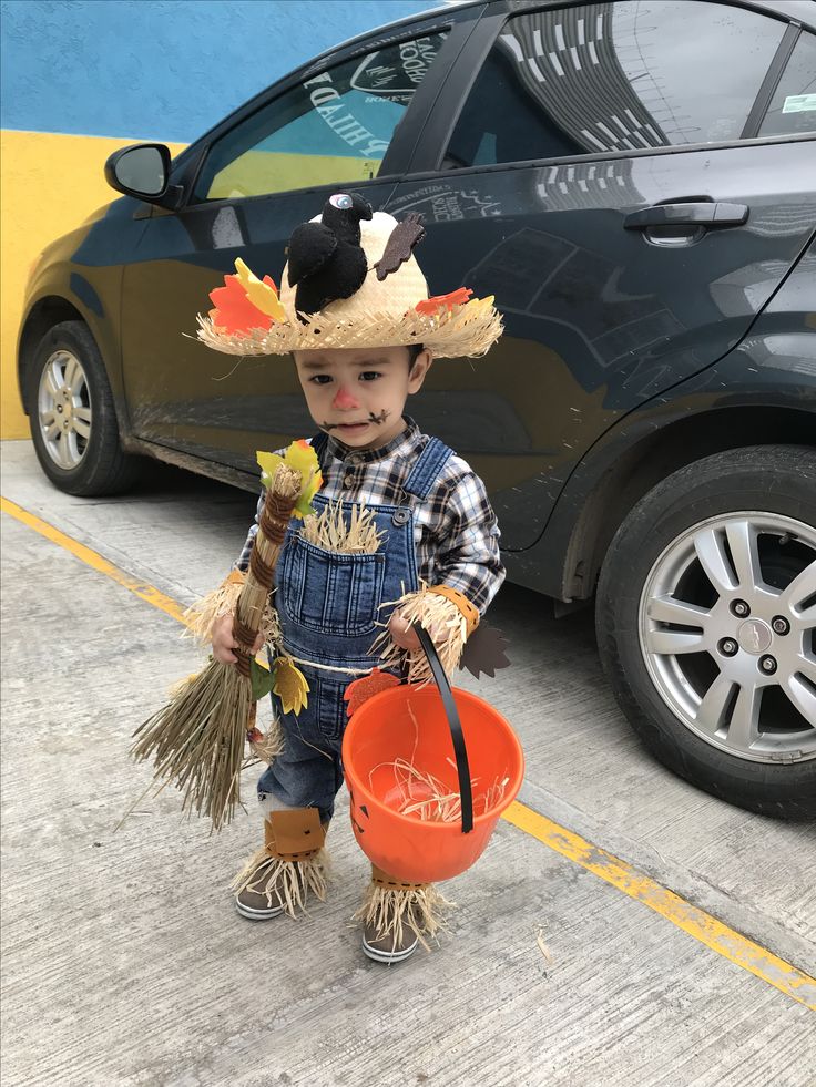 a little boy dressed up as a scarecrow holding a bucket and a broom in front of a car