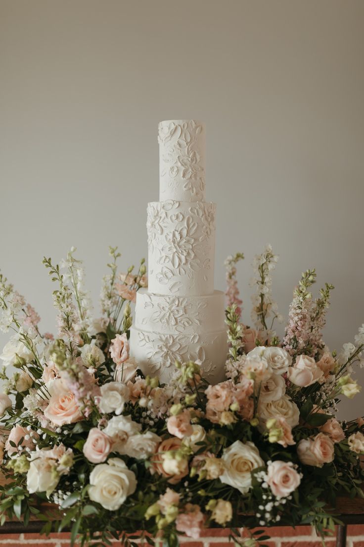 a white wedding cake sitting on top of a table next to flowers and greenery