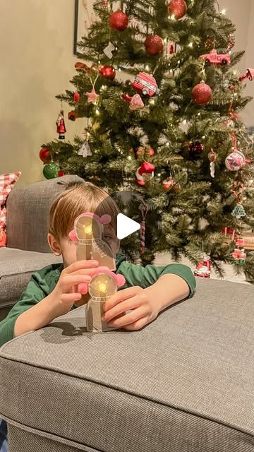 a little boy sitting on top of a couch next to a christmas tree with lights