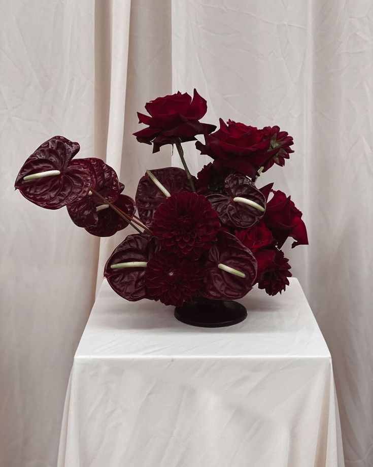 a vase filled with red flowers sitting on top of a white tablecloth covered table