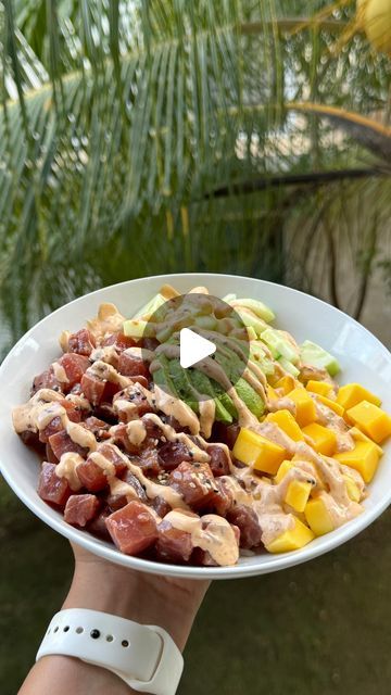 a person holding a white plate with meat and fruit on it in front of palm trees