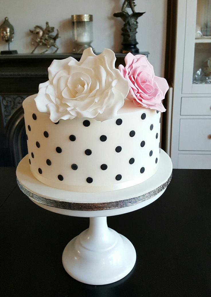 a polka dot cake with pink and white flowers on top, sitting on a black table