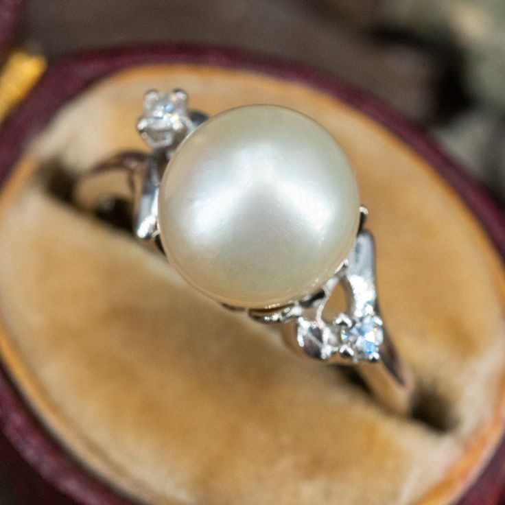 This pretty ring features a cultured pearl and two round single cut diamonds and is crafted of 14k white gold. This ring is currently a size 5.5. The pearl is slightly abraded. Formal Oval Pearl Ring, Classic Pearl Ring With Single Diamond, Classic Pearl Ring With Single Diamond For Anniversary, Heirloom White Gold Pearl Ring For Anniversary, Exquisite Oval White Gold Pearl Ring, Oval White Gold Pearl Ring For Anniversary, White Gold Heirloom Pearl Ring For Formal Occasions, Classic Oval Akoya Pearl Ring, Elegant Pear-shaped Ring With Single Diamond