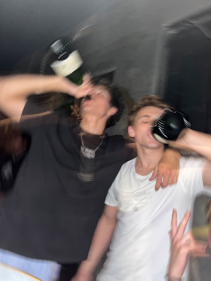 three young men standing next to each other with their hands in the air and one holding a wine bottle