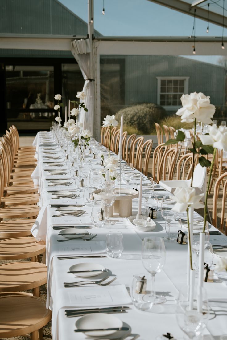 a long table is set up with white flowers and place settings for an elegant dinner