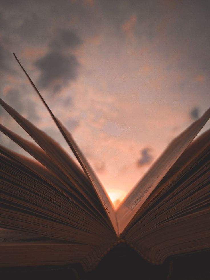 an open book sitting on top of a table next to a sky filled with clouds