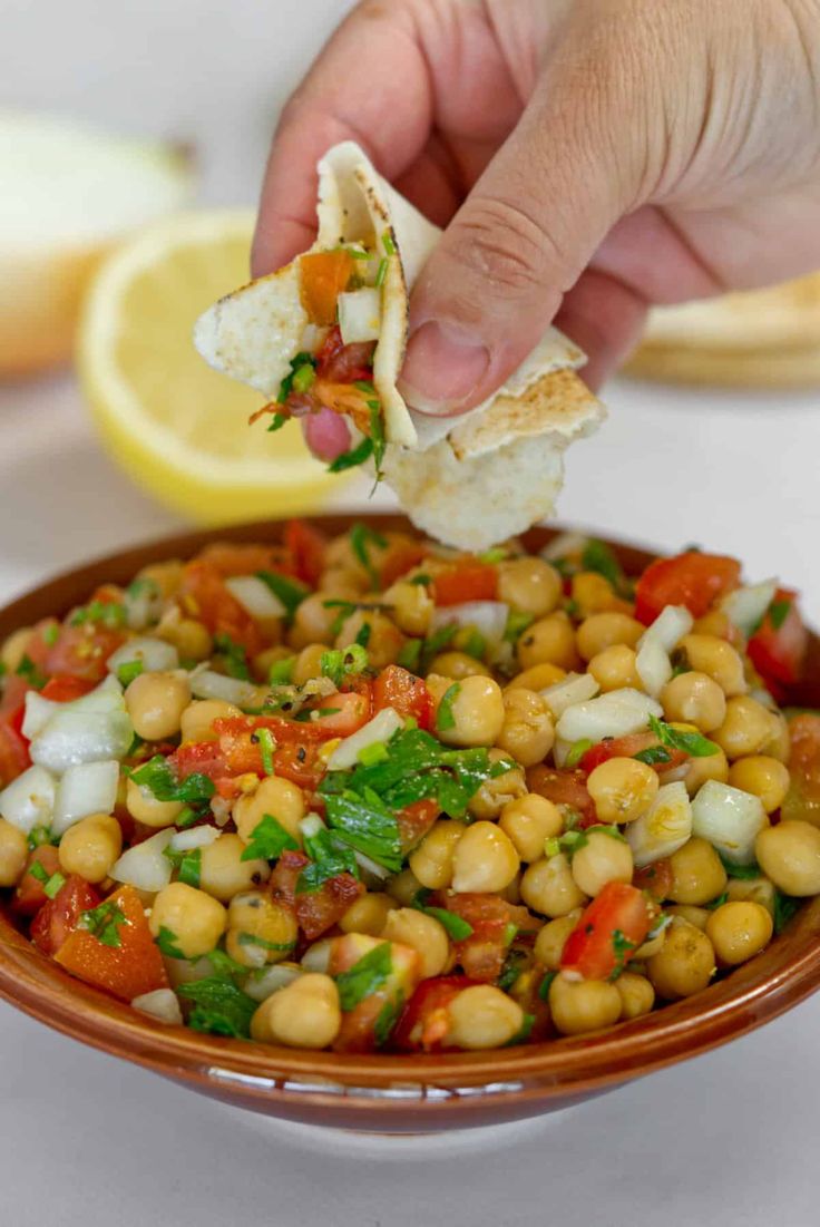 a person holding a tortilla over a bowl filled with chickpeas and vegetables