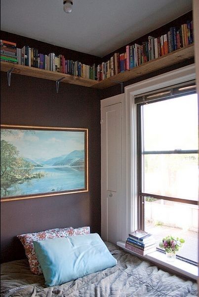 a bed sitting under a window next to a book shelf with books on top of it