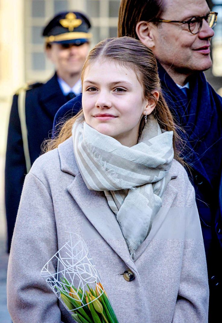 a woman in a coat and scarf holding flowers