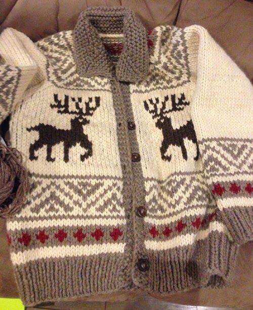 a sweater with moose on it is sitting on a couch next to a ball of yarn