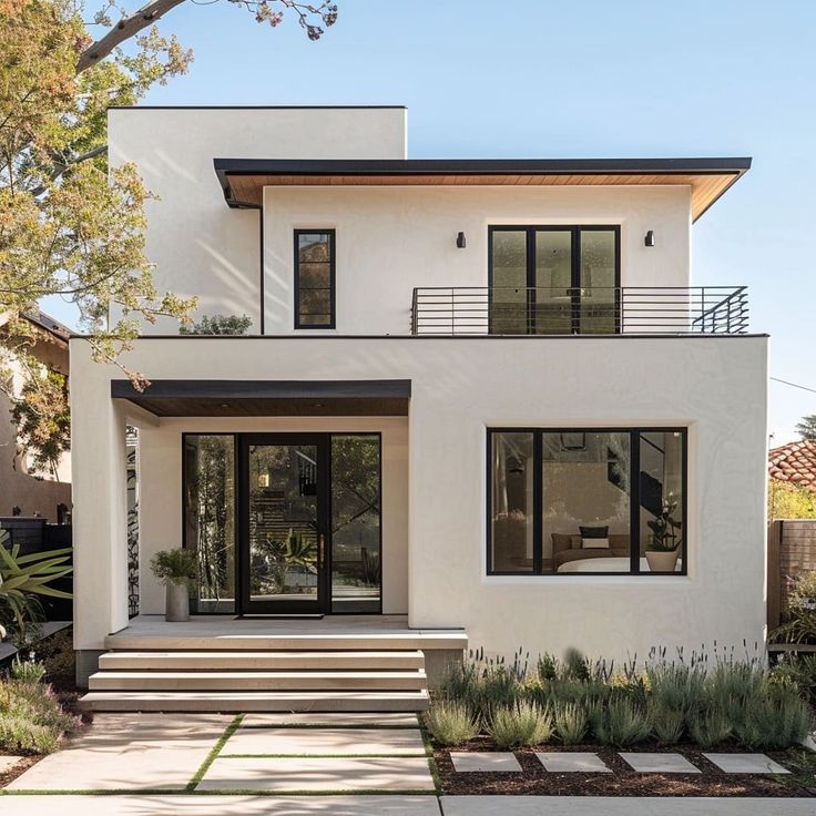 a white house with black windows and steps leading up to the front door is surrounded by greenery