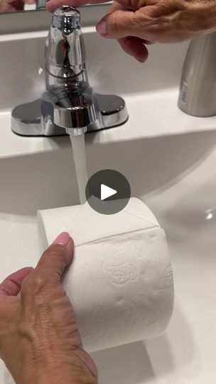 two hands are holding a roll of toilet paper in front of a sink with the faucet running