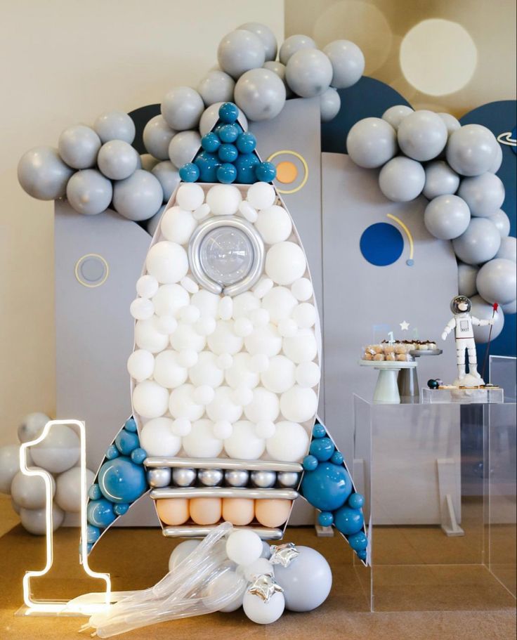 a rocket ship made out of balloons on a table next to some white and blue decorations