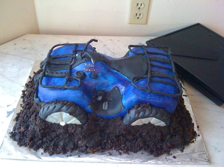 a cake that looks like a monster truck is on top of some dirt and has blue frosting