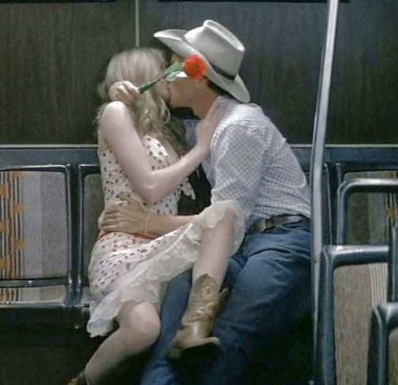 a man kissing a woman on the cheek while sitting in a bus seat with a flower in his mouth