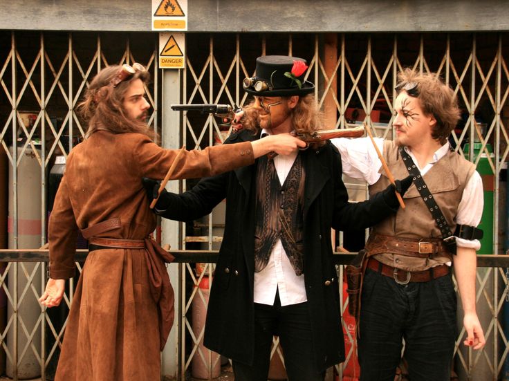 three men dressed in pirate costumes standing next to each other on the street with swords