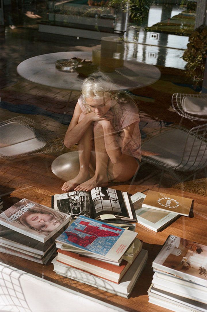 a woman sitting on the floor next to a pile of books in front of a window