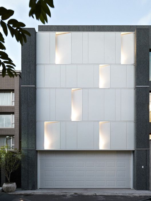 a white and grey building with lights on it's windows in front of a tree