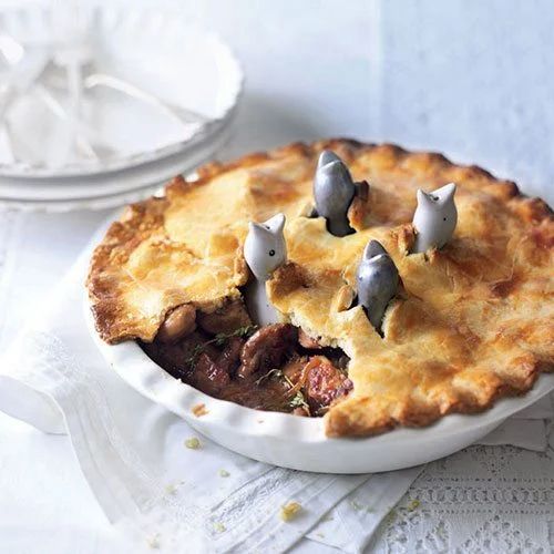 a pie with little birds on top is sitting on a white tablecloth next to plates