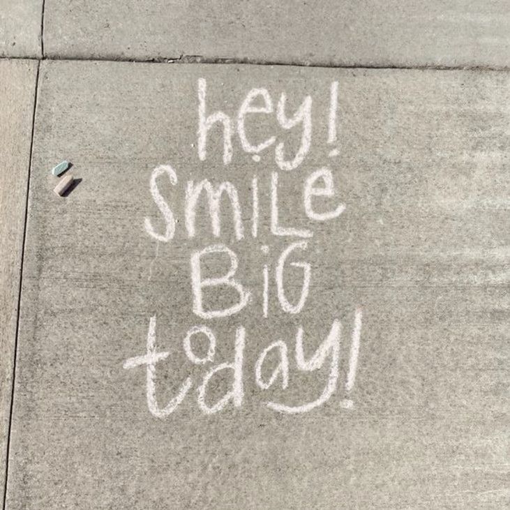 someone wrote this message on the sidewalk to say hey, smile big today in white chalk